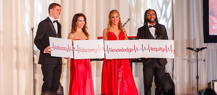 Photo of four people holding up a banner reading equity, knowledge, discovery, and advocacy with each word separated by an EKG reading.